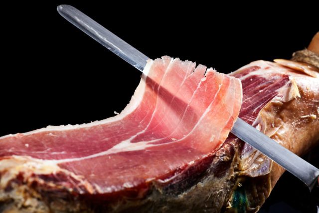 Long knife cutting into a piece of prosciutto