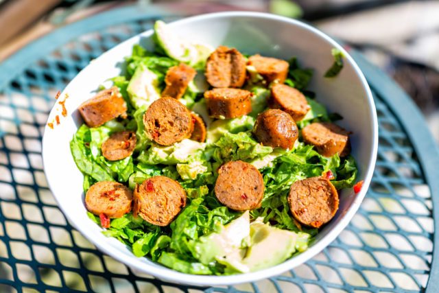 Closeup of fresh chopped vegetable romaine lettuce salad with greens avocado and Italian sausage on table healthy lunch meal