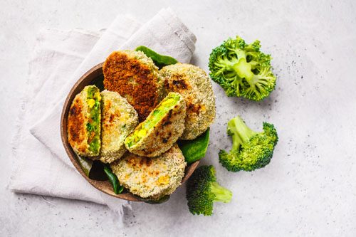 Green broccoli burgers in coconut shell dish on white background, top view.