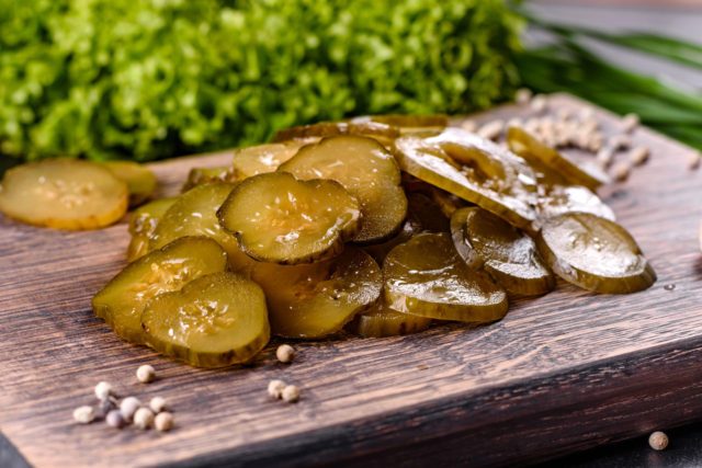 Tasty salty spicy pickled cucumber cut with rings on a wooden cutting board